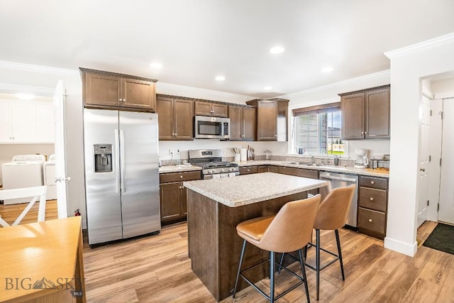 708 Pierre St, Belgrade, MT 59714 - kitchen featuring stainless steel appliances, washing machine and dryer, ornamental molding, a center island, and light wood-type flooring