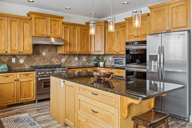 3609 Fieldstone W, Bozeman, MT 59715 - kitchen featuring appliances with stainless steel finishes, under cabinet range hood, light wood-type flooring, brown cabinets, and a kitchen island