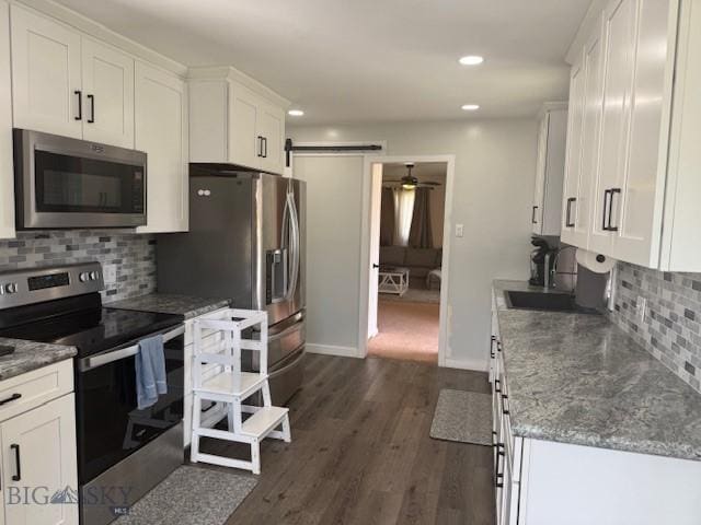 306 Juniper St, Anaconda, MT 59711 - kitchen featuring appliances with stainless steel finishes, white cabinetry, a barn door, tasteful backsplash, and dark wood finished floors