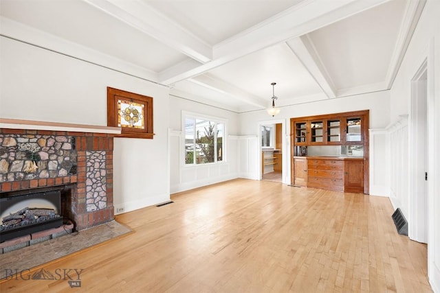 1039 Placer St, Butte, MT 59701 - unfurnished living room with light wood-type flooring, beam ceiling, a fireplace with raised hearth, a decorative wall, and wainscoting