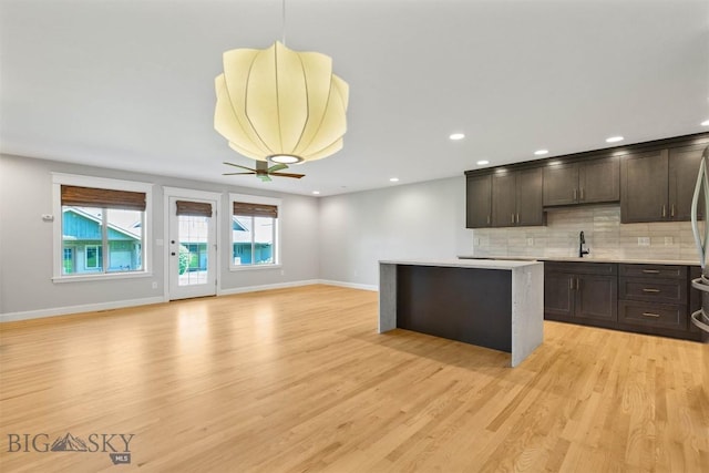 2757 Marlyn Ct Unit 1, Bozeman, MT 59718 - kitchen with dark brown cabinetry, a kitchen island, tasteful backsplash, light wood-style flooring, and light countertops