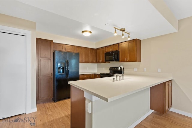 210 S Cottonwood Rd Unit 308, Bozeman, MT 59718 - kitchen featuring black appliances, light wood-style floors, a peninsula, light countertops, and brown cabinetry