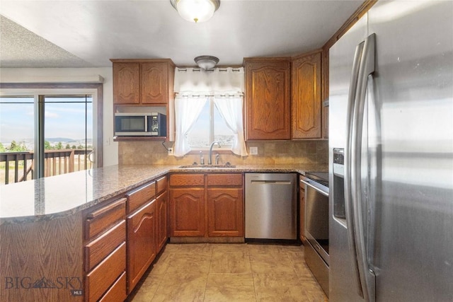 34 Mammoth Dr, Butte, MT 59701 - kitchen featuring stainless steel appliances, a peninsula, tasteful backsplash, brown cabinets, and light stone counters