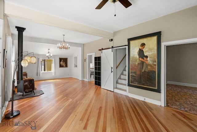 606 S Washington St, Dillon, MT 59725 - unfurnished living room featuring a wood stove, a barn door, ceiling fan, light wood-type flooring, and a chandelier