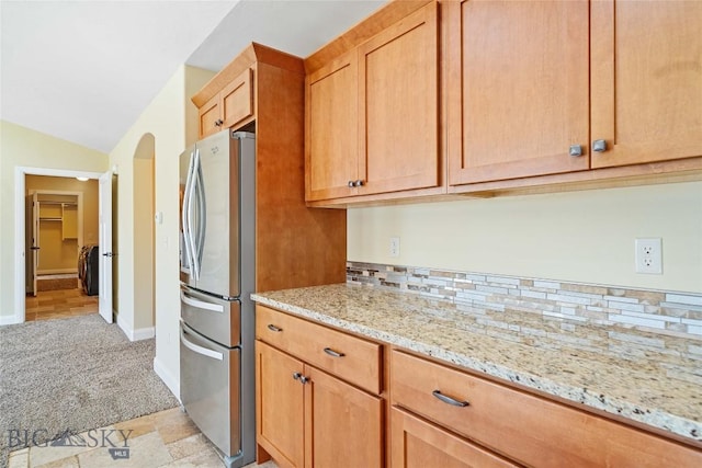 1705 Ingomar Blvd, Belgrade, MT 59714 - kitchen featuring freestanding refrigerator, light carpet, light stone counters, arched walkways, and vaulted ceiling
