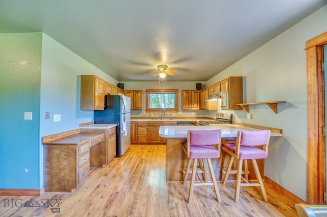 8799 Huffman Ln, Bozeman, MT 59715 - kitchen featuring stainless steel gas stove, freestanding refrigerator, a peninsula, light wood-type flooring, and light countertops