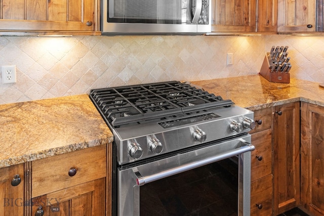58 Upper Moose Hill Rd, Big Sky, MT 59716 - kitchen featuring appliances with stainless steel finishes, brown cabinets, backsplash, and light stone counters