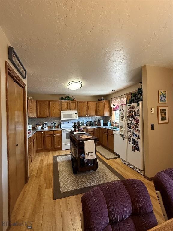 19970 Mt Highway 91 N, Glen, MT 59732 - kitchen featuring white appliances, light wood-type flooring, brown cabinetry, a textured ceiling, and light countertops