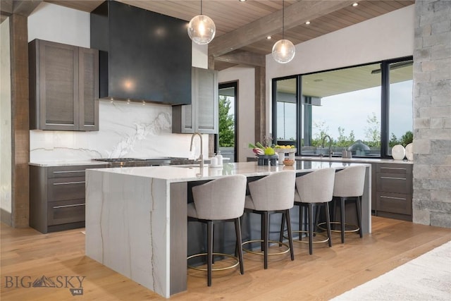 240 Horsetail Rd, Bozeman, MT 59715 - kitchen with a kitchen island with sink, light wood finished floors, a wood ceiling with exposed beams, exhaust hood, and a breakfast bar