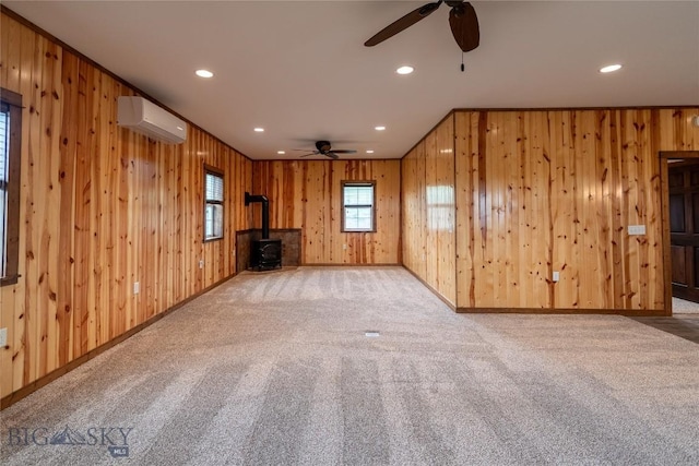 115 Otter Creek Rd, Big Timber, MT 59011 - unfurnished living room with a wall mounted air conditioner, ceiling fan, a wood stove, wood walls, and carpet