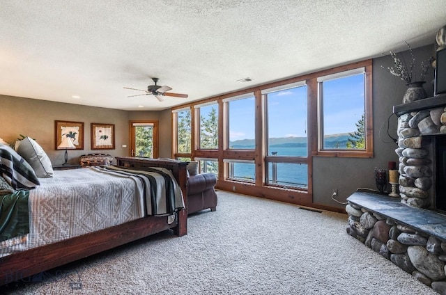 953 Angel Point Rd, Lakeside, MT 59922 - carpeted bedroom with a textured ceiling, a water view, a ceiling fan, and a stone fireplace