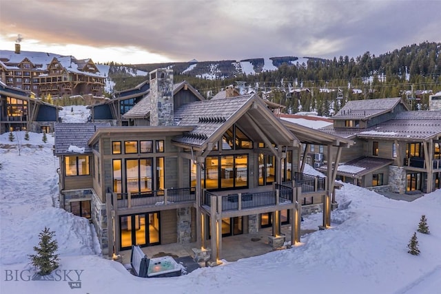 snow covered rear of property featuring stone siding and a chimney