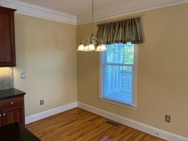 unfurnished dining area featuring ornamental molding, hardwood / wood-style floors, and an inviting chandelier