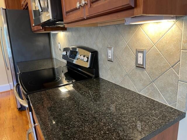 kitchen featuring backsplash, appliances with stainless steel finishes, dark stone countertops, and wood-type flooring