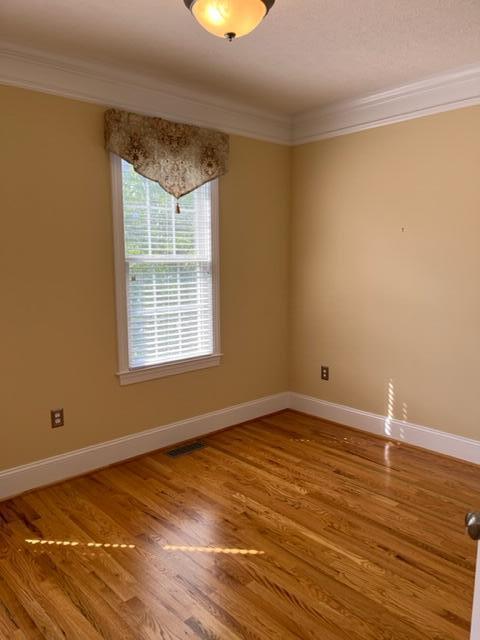 empty room with ornamental molding, a healthy amount of sunlight, and wood-type flooring