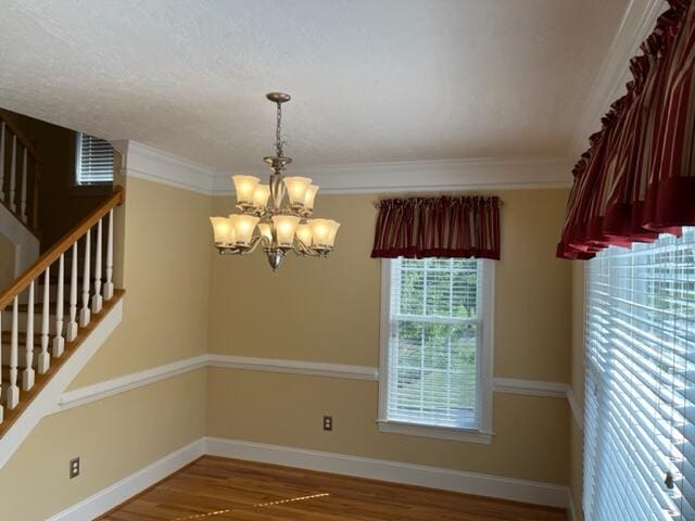 empty room featuring a notable chandelier, wood-type flooring, and crown molding