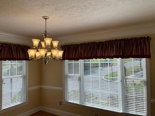 interior space featuring an inviting chandelier, a textured ceiling, and ornamental molding