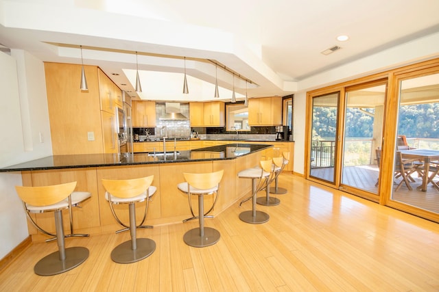 kitchen featuring dark stone countertops, pendant lighting, wall chimney range hood, sink, and a kitchen breakfast bar