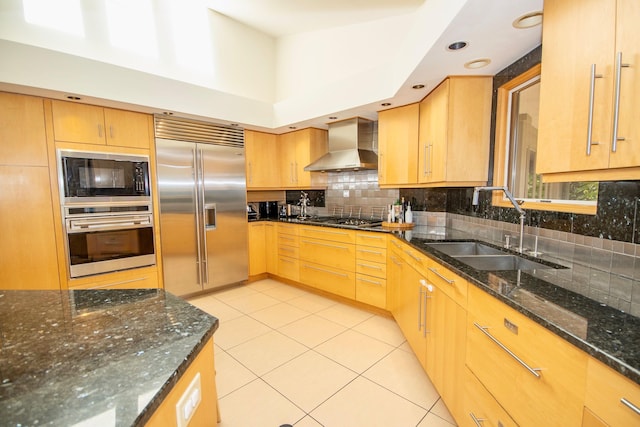 kitchen with tasteful backsplash, built in appliances, dark stone countertops, wall chimney range hood, and sink