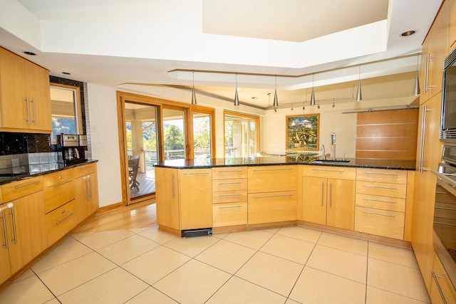 kitchen featuring light tile flooring, dark stone countertops, sink, hanging light fixtures, and a tray ceiling