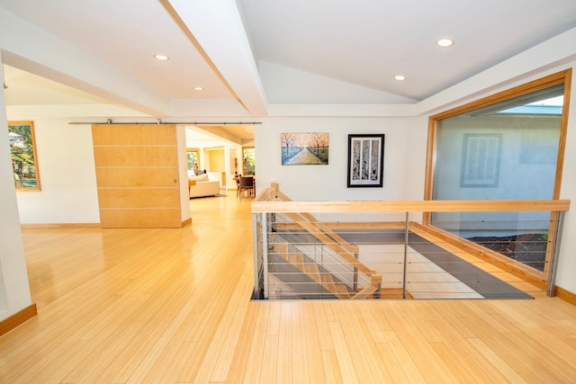 corridor with a barn door, vaulted ceiling with beams, and light hardwood / wood-style flooring