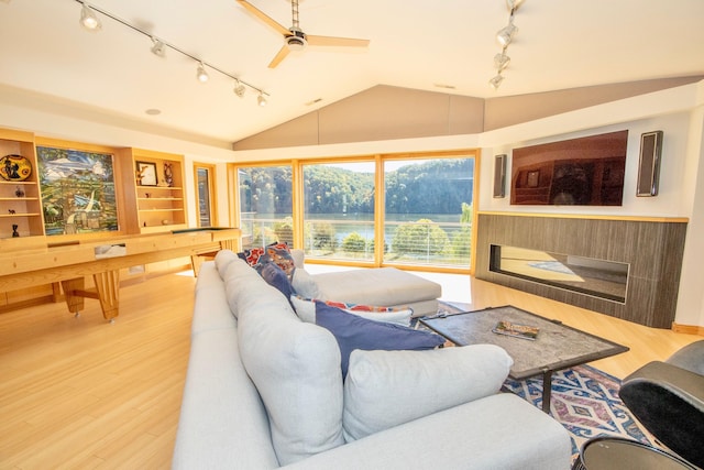 living room featuring rail lighting, ceiling fan, vaulted ceiling, and light wood-type flooring