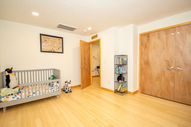 bedroom with light hardwood / wood-style floors, a closet, and a crib