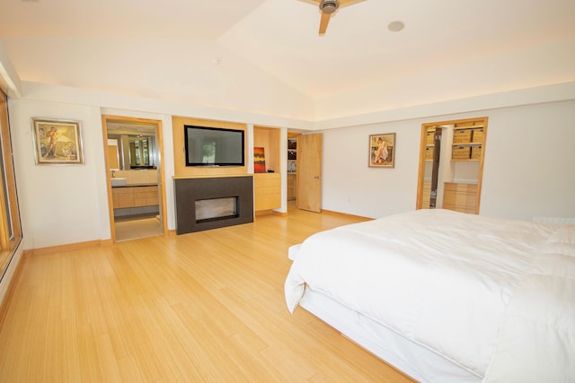 bedroom featuring light hardwood / wood-style floors, connected bathroom, vaulted ceiling, and ceiling fan