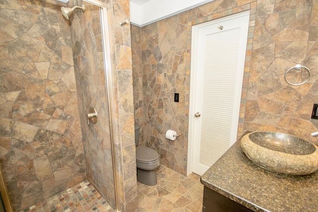 bathroom with tile walls, toilet, vanity, and tiled shower