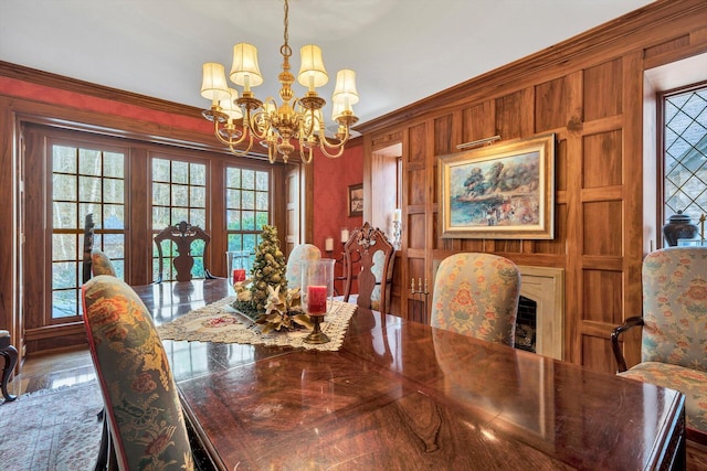 dining room featuring plenty of natural light, crown molding, wood walls, and a chandelier