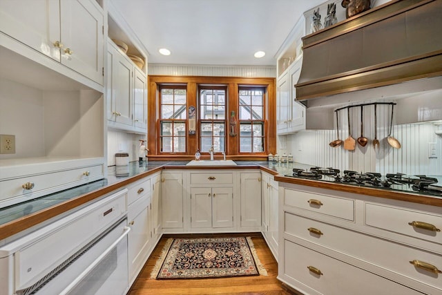 kitchen with premium range hood, stainless steel gas stovetop, light hardwood / wood-style flooring, white cabinets, and sink