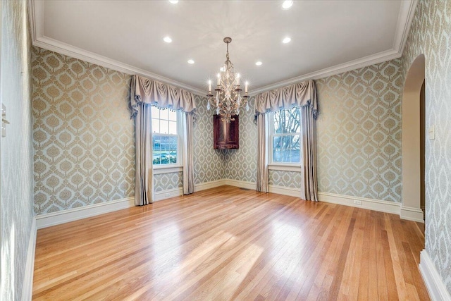 empty room with crown molding, a notable chandelier, and light wood-type flooring