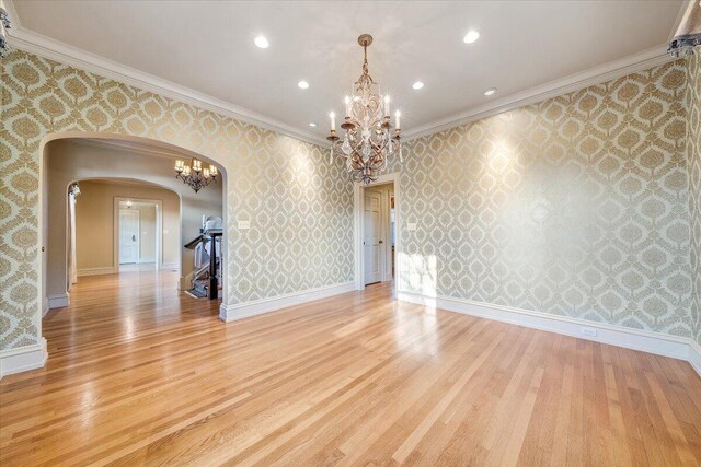 empty room featuring ornamental molding, light wood-type flooring, and an inviting chandelier