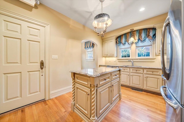 kitchen with decorative light fixtures, a center island, light stone countertops, light hardwood / wood-style flooring, and stainless steel refrigerator