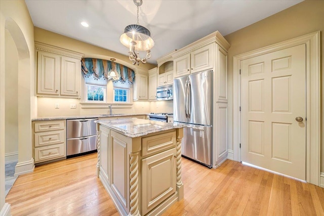 kitchen featuring appliances with stainless steel finishes, light wood-type flooring, a center island, and decorative light fixtures