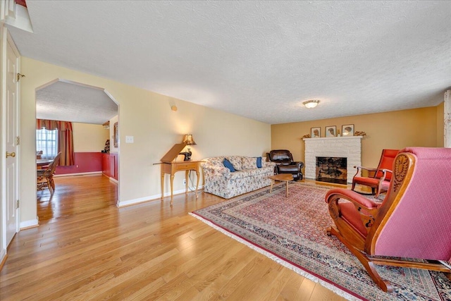 living room with a textured ceiling, a brick fireplace, and light wood-type flooring