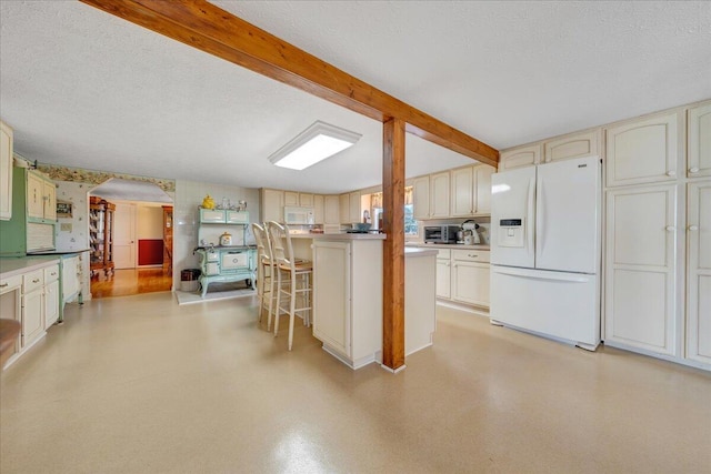 kitchen with beam ceiling, white appliances, a kitchen bar, and a textured ceiling