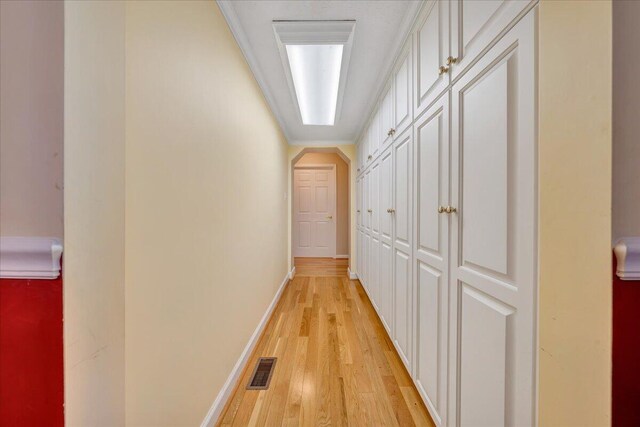 hallway with light wood-type flooring and ornamental molding