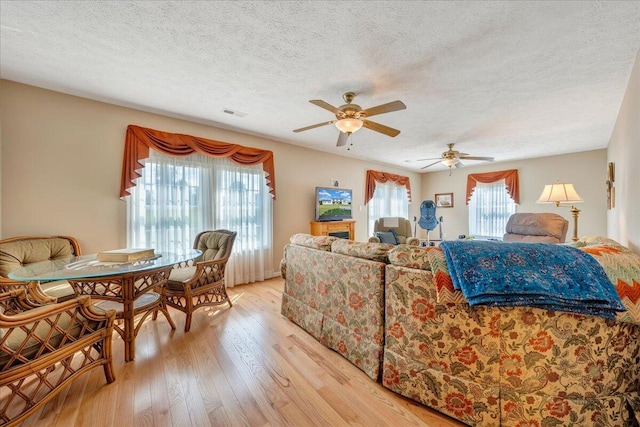 living room featuring ceiling fan, light wood-type flooring, and a textured ceiling