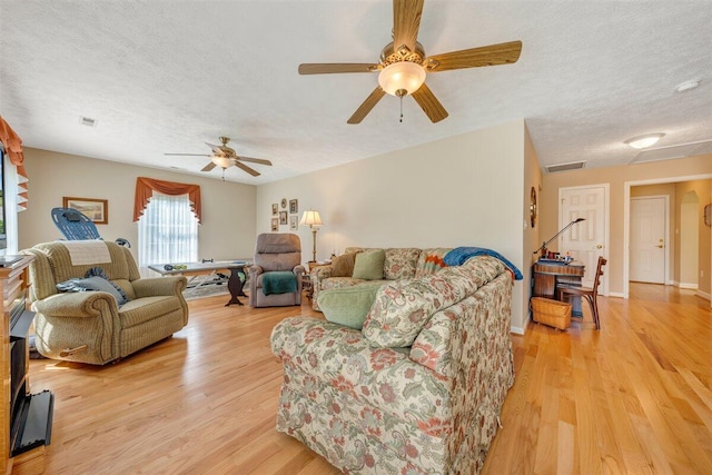 living room with light hardwood / wood-style floors, ceiling fan, and a textured ceiling