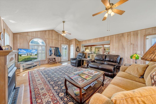 living room with wooden walls, vaulted ceiling, ceiling fan, and light hardwood / wood-style floors