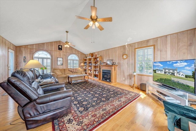 living room featuring ceiling fan, lofted ceiling, light hardwood / wood-style flooring, and wooden walls