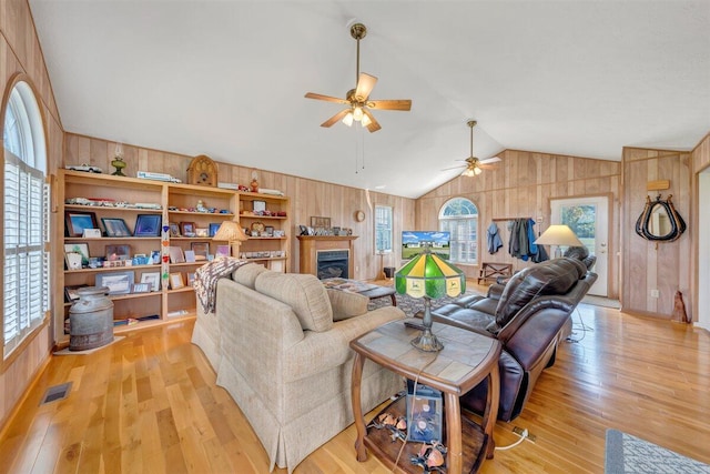 living room with ceiling fan, light hardwood / wood-style floors, wooden walls, and vaulted ceiling