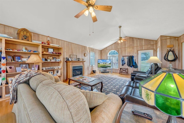 living room with wooden walls, light hardwood / wood-style floors, ceiling fan, and vaulted ceiling