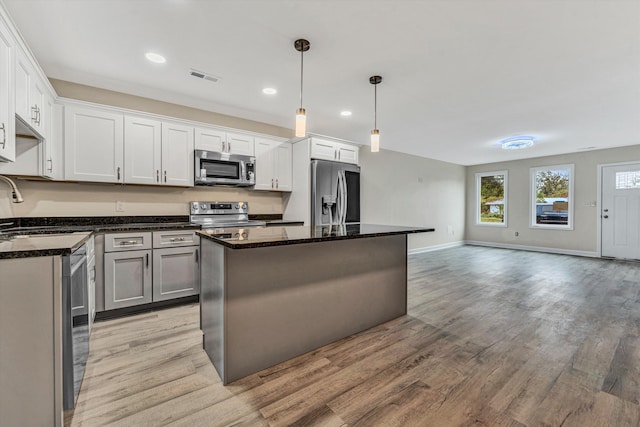 kitchen with appliances with stainless steel finishes, sink, white cabinets, a kitchen island, and hanging light fixtures