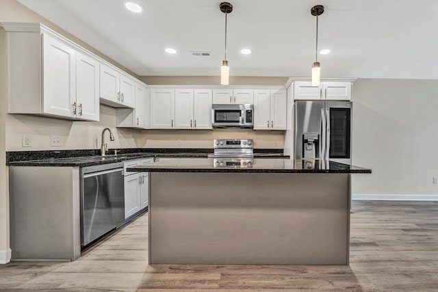 kitchen featuring dark stone counters, stainless steel appliances, white cabinetry, a kitchen island, and hanging light fixtures