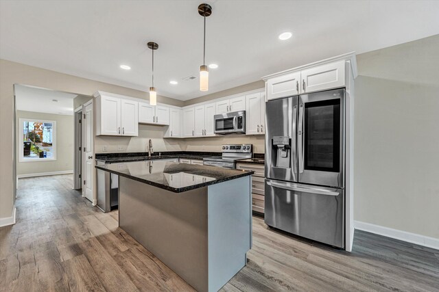 kitchen with appliances with stainless steel finishes, wood-type flooring, dark stone countertops, white cabinetry, and hanging light fixtures