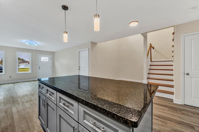 kitchen with pendant lighting, hardwood / wood-style flooring, a kitchen island, and dark stone counters