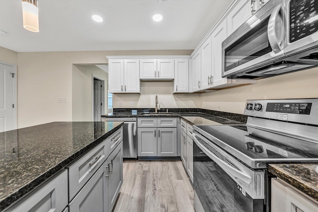 kitchen featuring appliances with stainless steel finishes, sink, white cabinets, light hardwood / wood-style floors, and hanging light fixtures