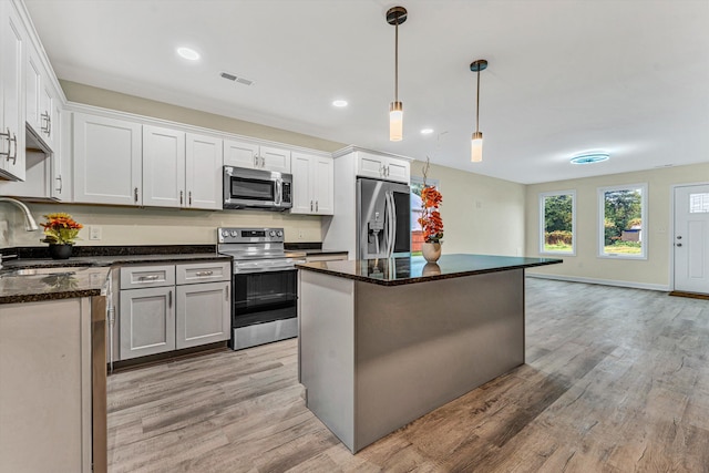 kitchen featuring sink, appliances with stainless steel finishes, decorative light fixtures, a kitchen island, and white cabinetry